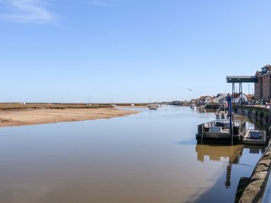 A river with boats docked along a stone quay and buildings in the background at Sunnyside in Wells-Next-The-Sea