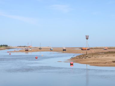A tidal river with several boats resting on sandbanks and red buoys at Sunnyside in Wells-Next-The-Sea