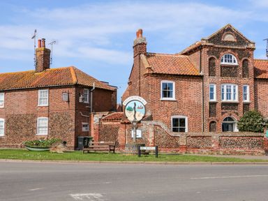 A street view with brick houses a wooden bench a boat planter and a Wells-Next-The-Sea sign at Sunnyside in Wells-Next-The-Sea