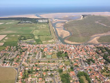 An aerial view of a coastal town with red-roofed houses green fields a river leading to the sea and sandy shorelines at Sunnyside in Wells-Next-The-Sea
