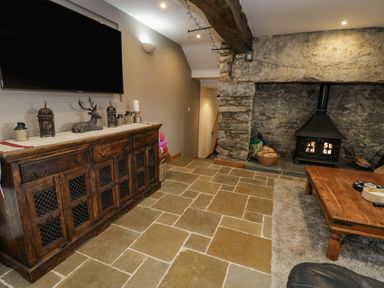 A living room with a mounted television above a wooden cabinet and a fireplace in a stone alcove at Hen Dy Craig Yr Ronwy in Capel Celyn near Bala