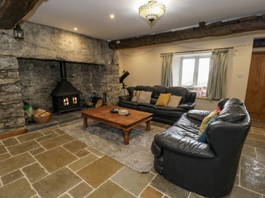 A living room with two leather sofas a wooden coffee table a stone fireplace and a window with curtains at Hen Dy Craig Yr Ronwy in Capel Celyn near Bala
