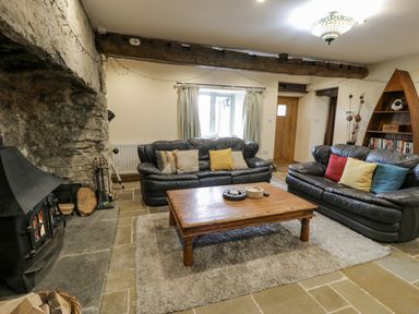 A living room with two black leather sofas a wooden coffee table a stone fireplace and a wooden bookshelf at Hen Dy Craig Yr Ronwy in Capel Celyn near Bala
