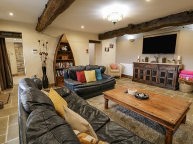A living room with black leather sofas a wooden coffee table a wooden cabinet with a TV mounted above and a boat-shaped bookshelf at Hen Dy Craig Yr Ronwy Capel Celyn near Bala
