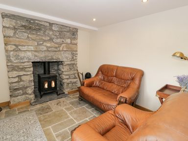 A living room with two brown leather sofas a stone fireplace with a black wood stove and a side table with flowers at Hen Dy Craig Yr Ronwy in Capel Celyn near Bala