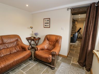A sitting room with two brown leather armchairs a wooden side table with a lamp and flowers and stone tile flooring at Hen Dy Craig Yr Ronwy in Capel Celyn near Bala