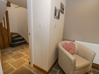 A corner hallway with stone tile floor a beige armchair with a heart shaped pink cushion a radiator and stairs with carpet