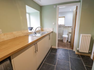 A kitchen with a sink and wooden countertop leading to a bathroom with a toilet at Hen Dy Craig Yr Ronwy Capel Celyn near Bala