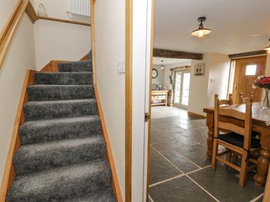A carpeted staircase next to a dining area with wooden furniture and stone tile flooring at Hen Dy Craig Yr Ronwy in Capel Celyn near Bala