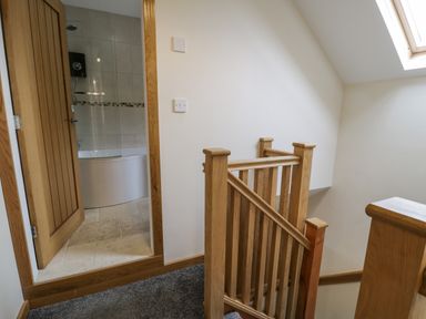 A staircase with wooden banisters next to a door leading to a bathroom with a bathtub at Hen Dy Craig Yr Ronwy in Capel Celyn near Bala