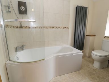 A bathroom with a white bathtub with a curved glass shower screen a toilet and a tall black radiator at Hen Dy Craig Yr Ronwy Capel Celyn near Bala