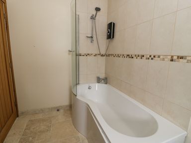 A bathroom with a bathtub a shower head and tiled walls at Hen Dy Craig Yr Ronwy in Capel Celyn near Bala
