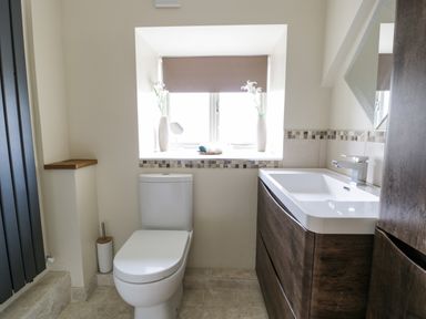 A bathroom with a toilet next to a wooden vanity and a window with a blind at Hen Dy Craig Yr Ronwy in Capel Celyn near Bala