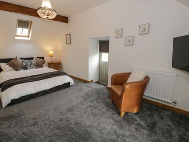 A bedroom with a bed side table and lamp a brown chair a wall mounted tv and framed pictures at Hen Dy Craig Yr Ronwy in Capel Celyn near Bala