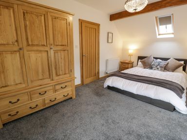 A bedroom with a wooden wardrobe a wooden door a bed with pillows and a blanket a bedside table with a lamp and a skylight window at Hen Dy Craig Yr Ronwy in Capel Celyn near Bala
