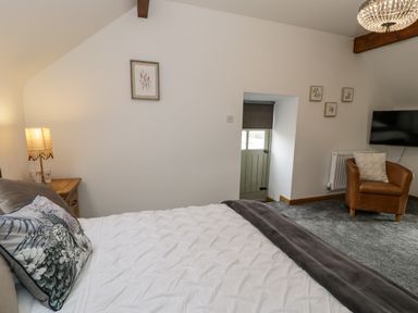A bedroom with a bed a bedside table with lamp a leather chair a wall-mounted television and framed pictures at Hen Dy Craig Yr Ronwy in Capel Celyn near Bala