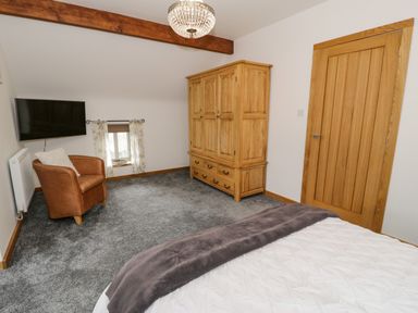 A bedroom with a wooden wardrobe a leather armchair a wall-mounted TV and a bed at Hen Dy Craig Yr Ronwy Capel Celyn near Bala