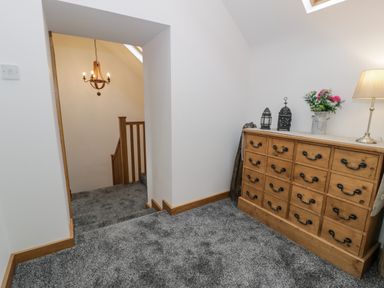 A hallway with gray carpet a wooden dresser a lamp flowers lanterns and a staircase with a chandelier at Hen Dy Craig Yr Ronwy in Capel Celyn near Bala