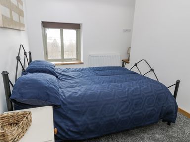 A bedroom with a double bed with blue bedding by a window at Hen Dy Craig Yr Ronwy in Capel Celyn near Bala