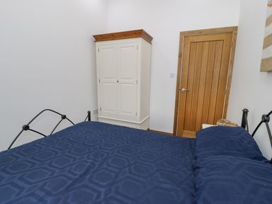 A bedroom with a blue bedspread on a black metal bed frame white wardrobe and a wooden door at Hen Dy Craig Yr Ronwy in Capel Celyn near Bala