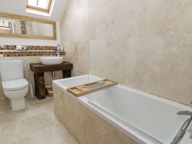 A bathroom with a toilet wooden sink counter bathtub with wooden tray and mirror at Hen Dy Craig Yr Ronwy in Capel Celyn near Bala