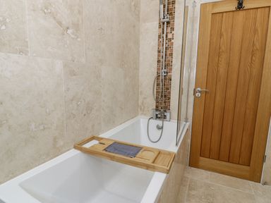 A bathroom with a bathtub shower wooden door and wooden bath tray at Hen Dy Craig Yr Ronwy in Capel Celyn near Bala