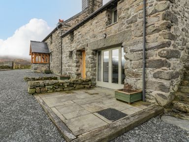 A stone building with a paved patio and planter boxes at Hen Dy Craig Yr Ronwy in Capel Celyn near Bala