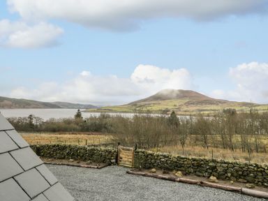 A gravel driveway with a stone wall and wooden gate overlooking a lake and a hill at Hen Dy Craig Yr Ronwy in Capel Celyn near Bala