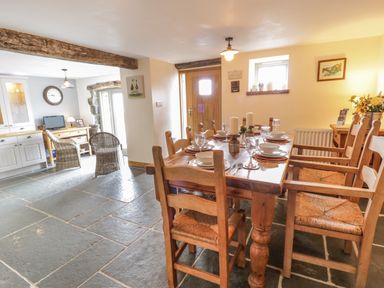 A dining area with a wooden table set with plates and glasses and wooden chairs in a room with stone flooring at Hen Dy Craig Yr Ronwy in Capel Celyn near Bala