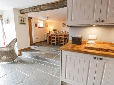 A kitchen with wooden countertop and white cabinets next to a dining area with wooden table and chairs at Hen Dy Craig Yr Ronwy in Capel Celyn near Bala