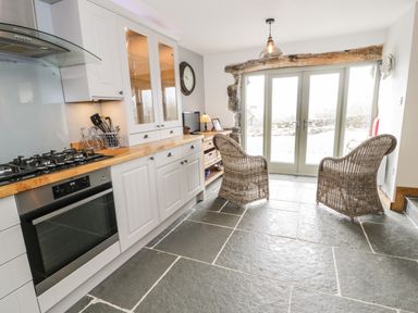 A kitchen with white cabinets wooden countertops a gas stove oven wicker chairs stone floor and glass doors at Hen Dy Craig Yr Ronwy Capel Celyn near Bala