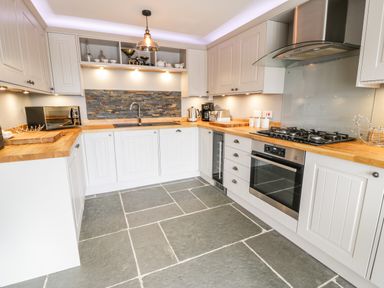 A kitchen with white cabinets wooden countertops a stone tile floor and stainless steel appliances at Hen Dy Craig Yr Ronwy in Capel Celyn near Bala