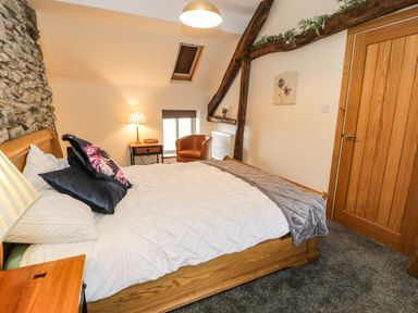A bedroom with a bed a bedside table a chair a lamp and a wooden door with exposed wooden beams at Hen Dy Craig Yr Ronwy in Capel Celyn near Bala