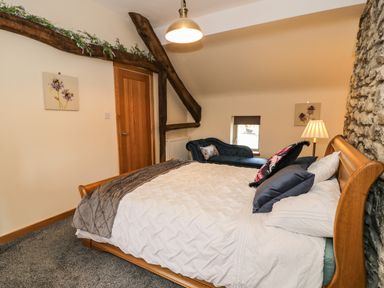 A bedroom with a wooden bed a navy chaise lounge and a stone wall at Hen Dy Craig Yr Ronwy in Capel Celyn near Bala