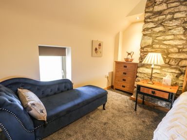 A room with a blue chaise lounge a wooden chest of drawers a bedside table with a lamp and a stone wall at Hen Dy Craig Yr Ronwy in Capel Celyn near Bala