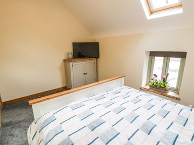 A bedroom with a bed a cabinet with a television and a window with flowers at Hen Dy Craig Yr Ronwy in Capel Celyn near Bala
