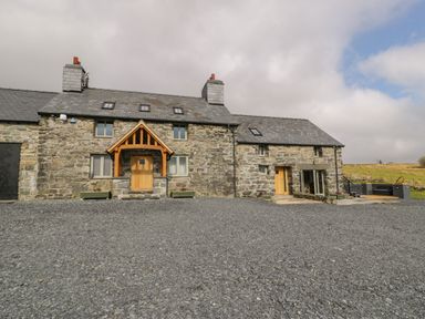 A stone house with wooden doors and a gravel driveway at Hen Dy Craig Yr Ronwy in Capel Celyn near Bala