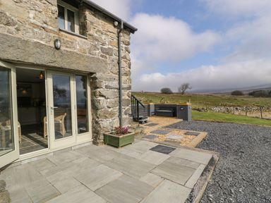 A stone house with glass doors opening to a patio and a garden area with a bench and gravel at Hen Dy Craig Yr Ronwy in Capel Celyn near Bala