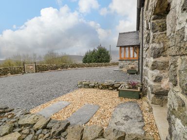 An outdoor area with stone walls gravel and flower planters beside a stone building at Hen Dy Craig Yr Ronwy in Capel Celyn near Bala