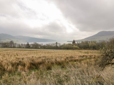 A field with dry grass trees a road a body of water and hills under a cloudy sky at Hen Dy Craig Yr Ronwy in Capel Celyn near Bala