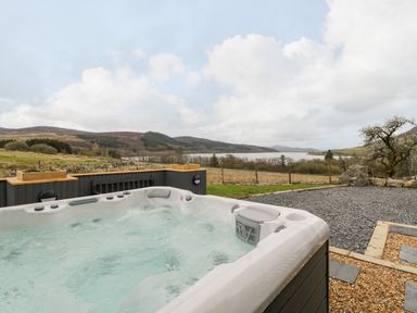 An outdoor hot tub with bubbling water overlooking a grassy field a lake and distant hills at Hen Dy Craig Yr Ronwy in Capel Celyn near Bala