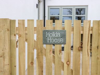 A wooden fence with a sign that reads Holida Hoose and a window on a white building behind the fence at Holida Hoose in Belford