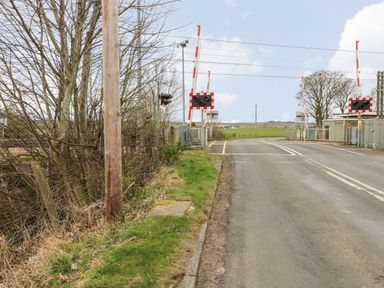 A railway level crossing with barriers and traffic lights on a rural road at Holida Hoose in Belford