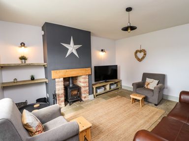 A living room with armchairs a wood burning stove a television and shelves at Holida Hoose in Belford