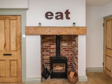A brick fireplace with a wood stove and wooden mantel with small plants and eat letters on the wall at Holida Hoose in Belford