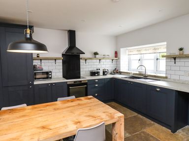 A kitchen with dark cabinets a wooden dining table and a black hanging lamp at Holida Hoose in Belford