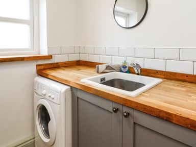 A laundry room corner with a washing machine under a wooden countertop a sink soap bottle and a round mirror on the wall at Holida Hoose in Belford