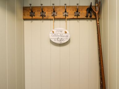 A wall with a wooden coat rack with five hooks and a sign hanging that says Its the little things in life at Holida Hoose in Belford