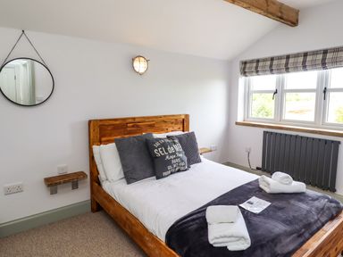 A bedroom with a wooden bed frame pillows and folded towels on the bed under a window at Holida Hoose in Belford