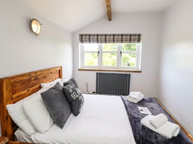 A bedroom with a wooden bed frame pillows blankets a window and a radiator at Holida Hoose in Belford